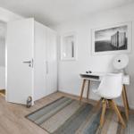 Ein Zimmer mit Schreibtisch, Stuhl und Kleiderschrank. Wandbild und Teppich sind sichtbar.