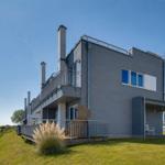 Moderne Villa mit Balkon, Garten und Blick auf Wasser.