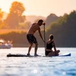 Drei Liegestühle mit Kissen stehen im Gras am Strand.