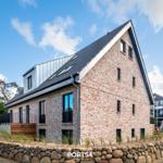 Ein modernes Haus mit Ziegelwand und Holzterrasse unter blauem Himmel.