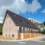 Moderne Villa mit Holzterrasse und Dachfenstern unter blauem Himmel.