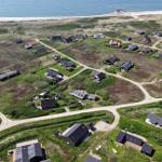 Aerial view of coastal village with scattered houses and winding dirt roads near the sea.