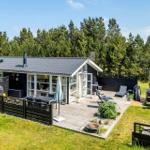 Ein dunkel verputztes Ferienhaus mit weißer Tür und Terrasse. Umgeben von Gras und Bäumen unter blauem Himmel.