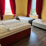 Zimmer mit drei Betten, gelben Wänden und roten Vorhängen.