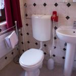 Badezimmer mit Toilette, Waschbecken und Fenster mit rotem Vorhang.