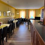 Großer Raum mit Essbereich, TV und Bar. Gelbe Wände, Holzboden und Fenster mit Vorhängen.