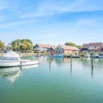 Houses by the harbor with boats and a dock. Green areas and clear view.