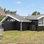 Black wooden cabin with grill and white gate in the garden.