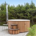 Backyard with wooden terrace, lounge chair, and hot tub between grass and trees.