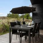 Black wooden cabin with terrace and hot tub in grassland.