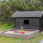 Black wooden house with terrace, grill area, and hot tub in grassland.