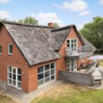 Red brick house with thatched roof and balcony. Garden area with grill and umbrella.
