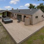 Modern wooden cabin with large deck, hot tub, and lounge area.