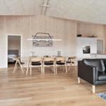 Living area with black leather furniture, wooden floor, and large window. Kitchen in the background.